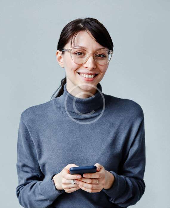Uśmiechnięta kobieta w okularach trzyma telefon komórkowy, szary sweter