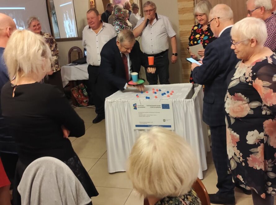 Grupa ludzi zebrała się wokół stołu z grą w pomieszczeniu.