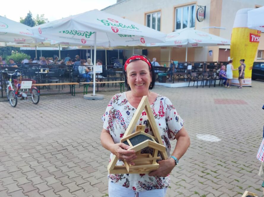 Kobieta w białych szortach trzyma drewniany karmnik na tle kawiarni.
