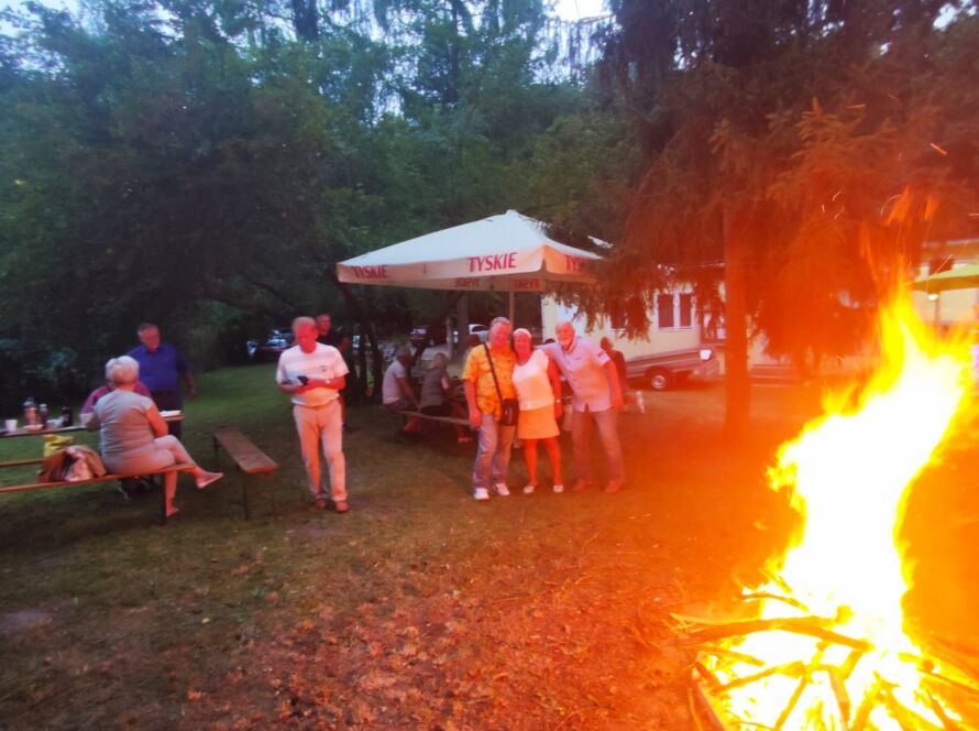 Grupa ludzi wokół ogniska na pikniku w ogrodzie.