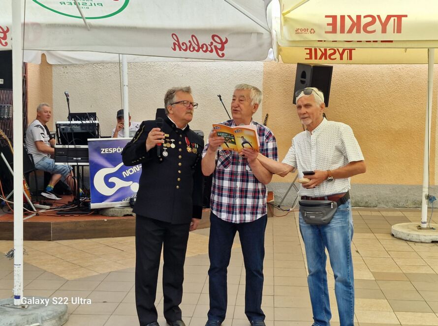 Trzej mężczyźni stojący pod parasolami podczas wydarzenia na świeżym powietrzu.