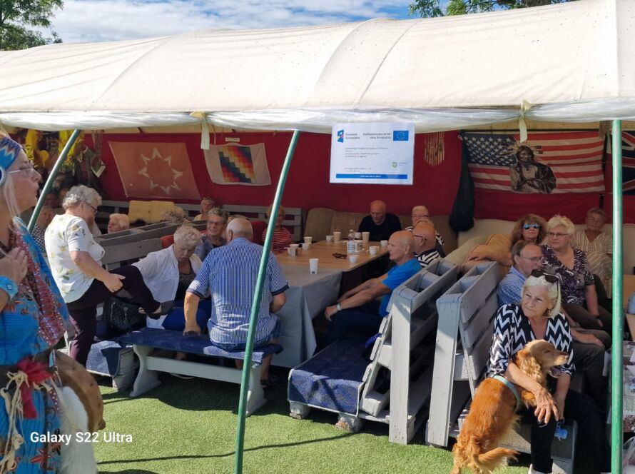 Grupa ludzi siedzących pod namiotem z flagami i dekoracjami.