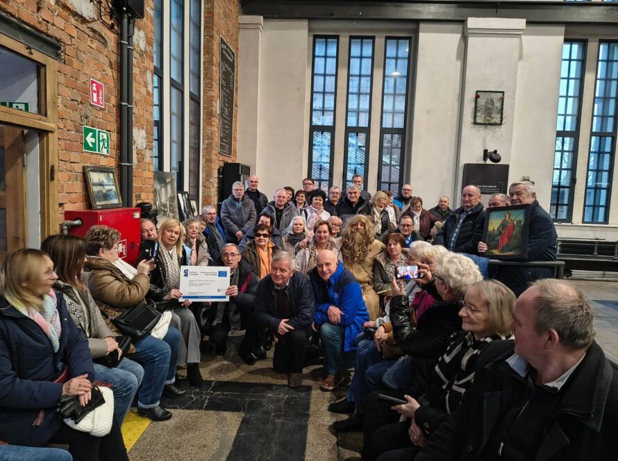 Grupa ludzi pozująca we wnętrzu, część trzyma certyfikat i obraz