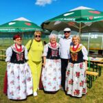 Osoby w tradycyjnych strojach śląskich na tle parasoli i ławek.