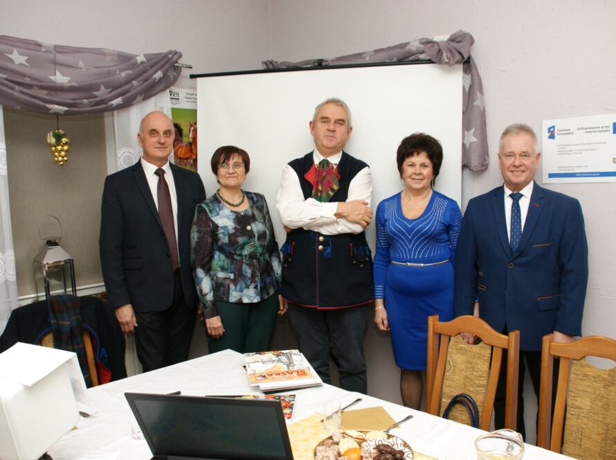Grupa pięciu osób w eleganckich strojach przy stole w sali konferencyjnej.