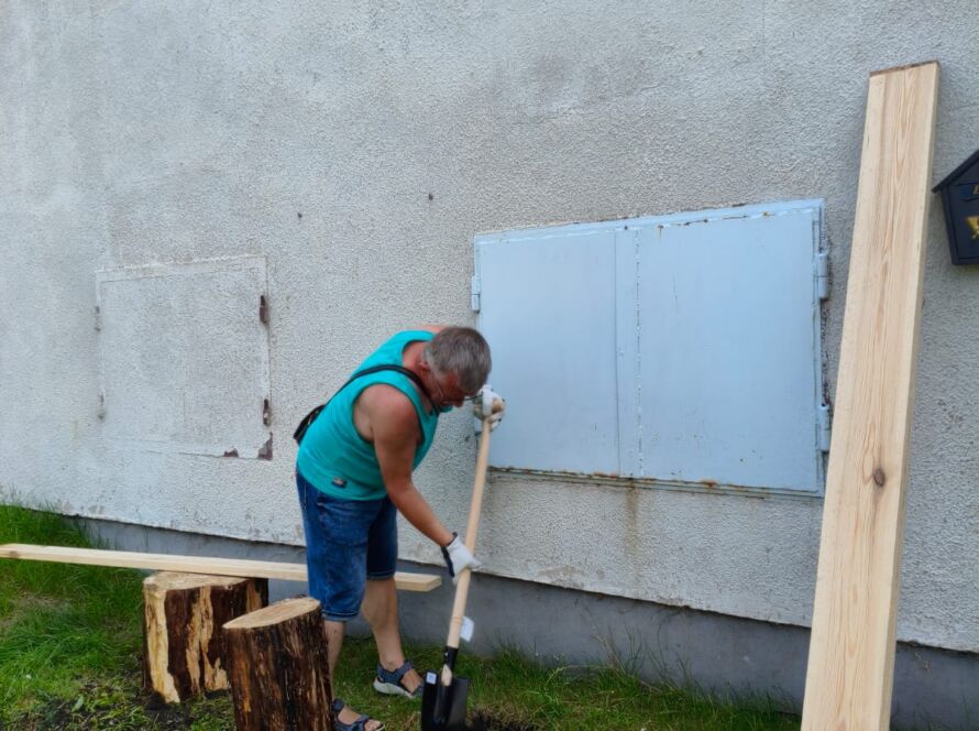 Osoba kopiąca łopatą przed budynkiem na trawie.
