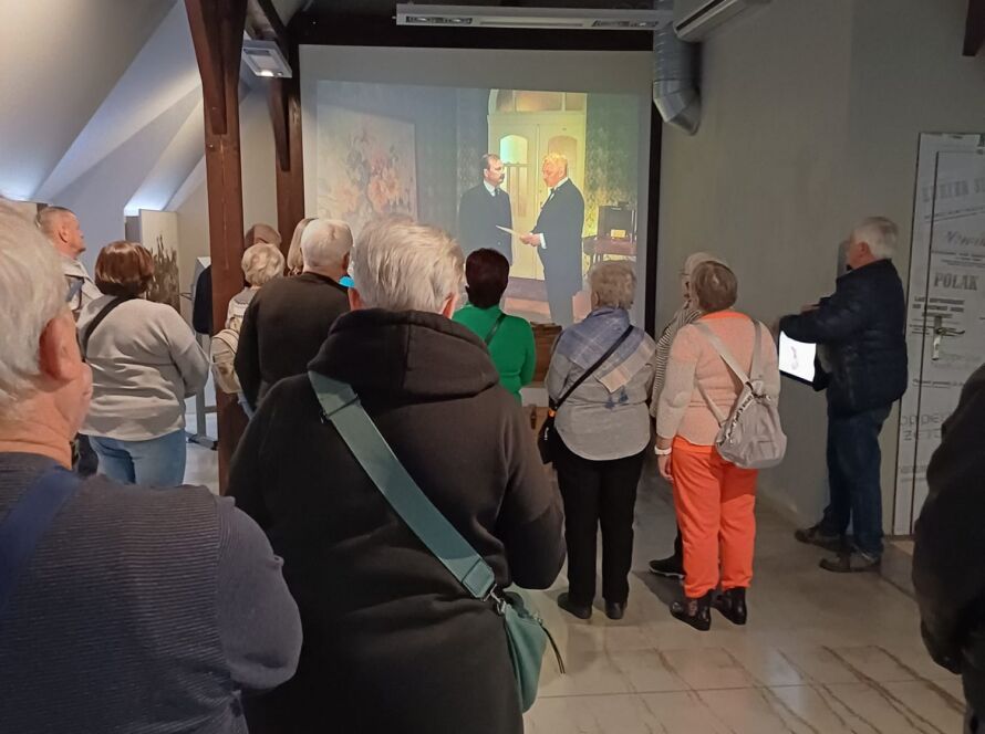Grupa zwiedzających ogląda projekcję filmu na ekranie w sali muzeum.