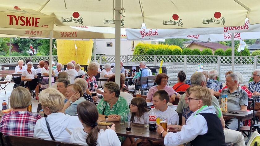 Grupa osób siedzących pod parasolami w ogrodzie piwnym.