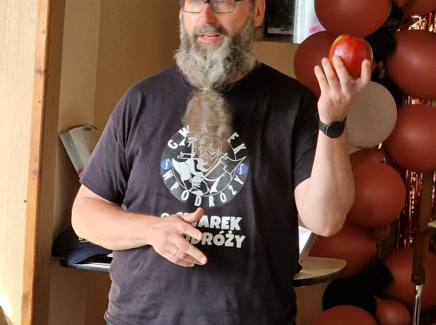 Mężczyzna z brodą trzymający jabłko, w tle balony