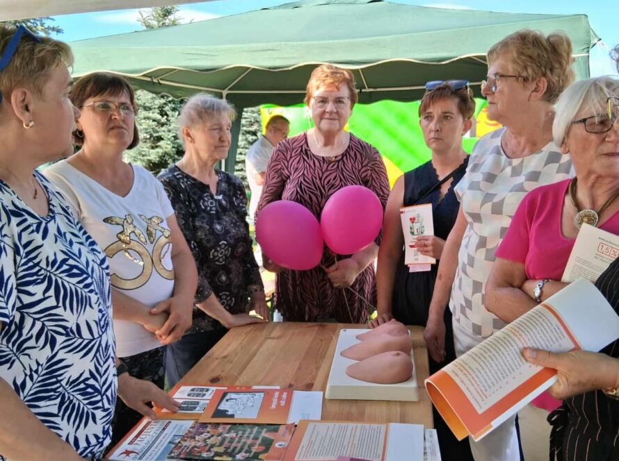 Grupa kobiet przy stoliku z ulotkami pod zielonym namiotem.