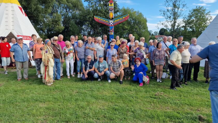 Grupa ludzi stojąca przed kolorowym totemem i tipis na trawie