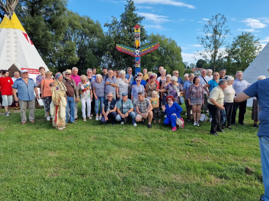 Grupa ludzi stojąca przed kolorowym totemem i tipis na trawie
