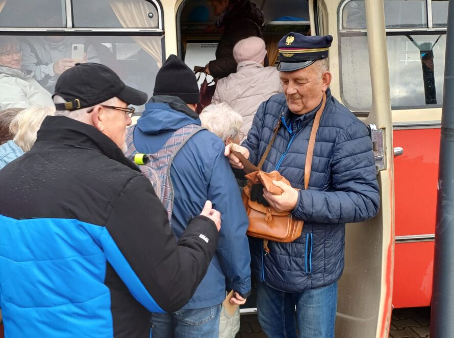 Konduktor w czapce sprawdza bilety pasażerom wsiadającym do zabytkowego autobusu