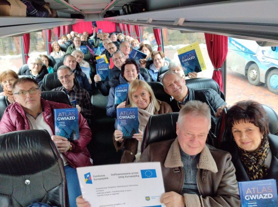 Grupa osób w autokarze z książkami 'Atlas Gwiazd' w rękach