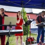 Trio muzyczne występujące na zewnątrz pod niebieskim namiotem