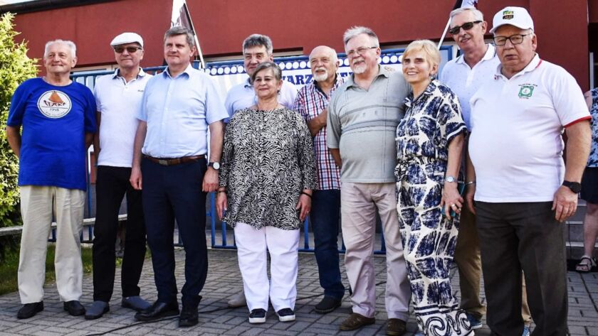Grupa starszych osób stojąca przed budynkiem sportowym.