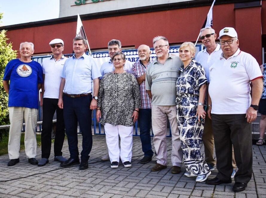 Grupa starszych osób stojąca przed budynkiem sportowym.