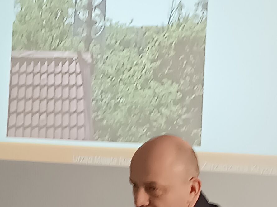 Mężczyzna przy stole, za nim prezentacja o systemie alarmowym.