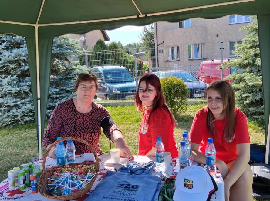 Trzy kobiety przy stoisku Polskiego Czerwonego Krzyża na zewnątrz.