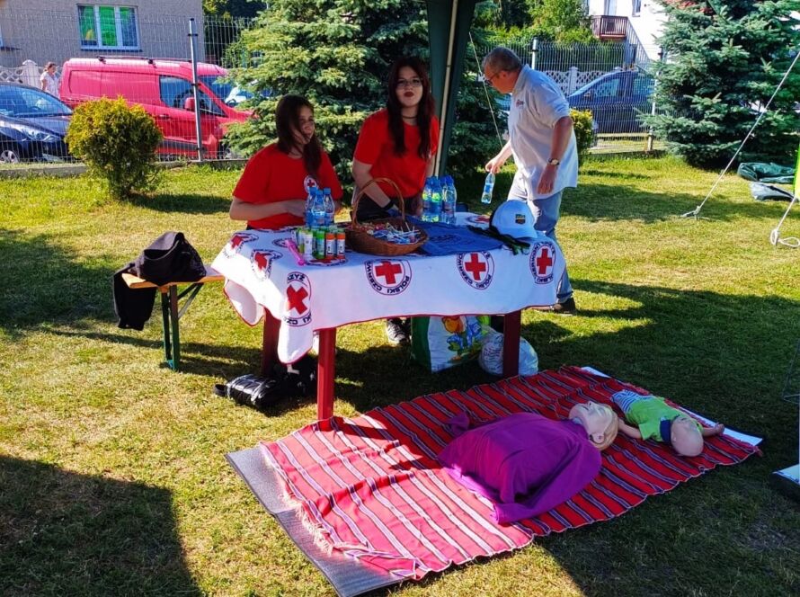 Stoisko Czerwonego Krzyża pod zielonym namiotem z manekinami do ćwiczeń.