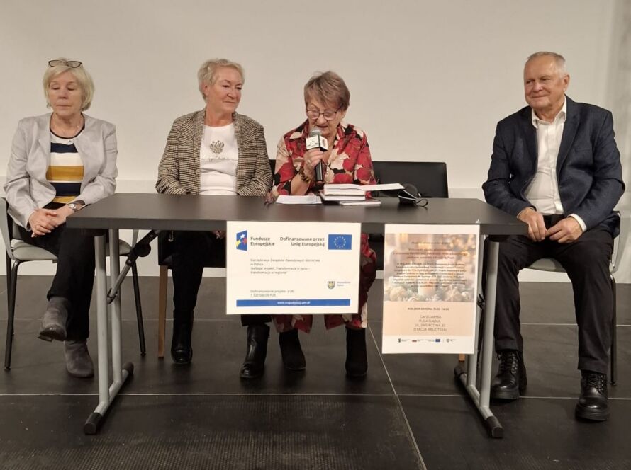 Cztery osoby siedzące przy stole na konferencji z mikrofonem.
