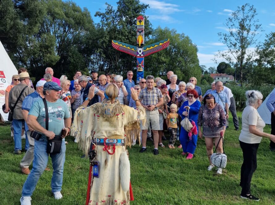 Grupa ludzi przed totemem na trawie podczas wydarzenia na świeżym powietrzu