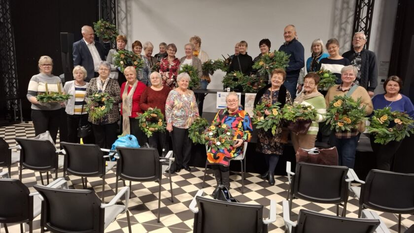 Grupa osób z wieńcami i ozdobami na warsztatach artystycznych