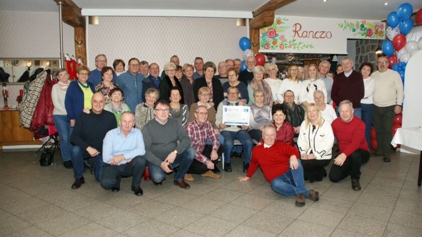 Duża grupa ludzi pozuje do zdjęcia w sali udekorowanej balonami.